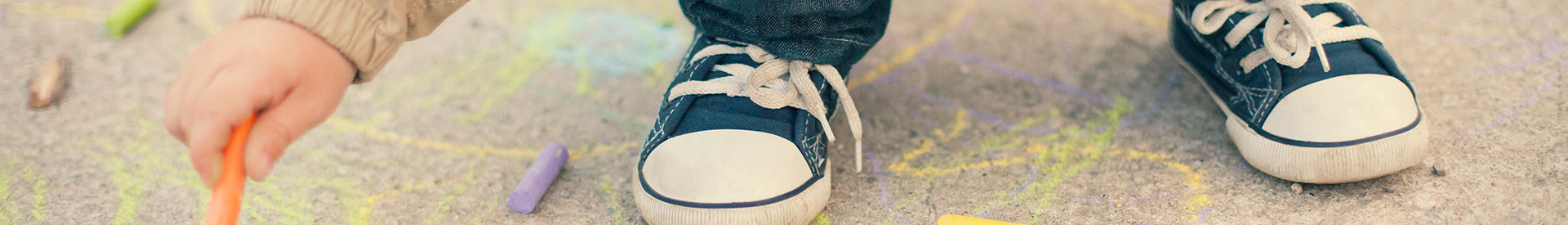 Child's hand drawing with chalk while he squats on the ground